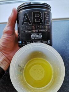 Op deze foto zie je de ABE Pre-Workout  en een scoop in een beker